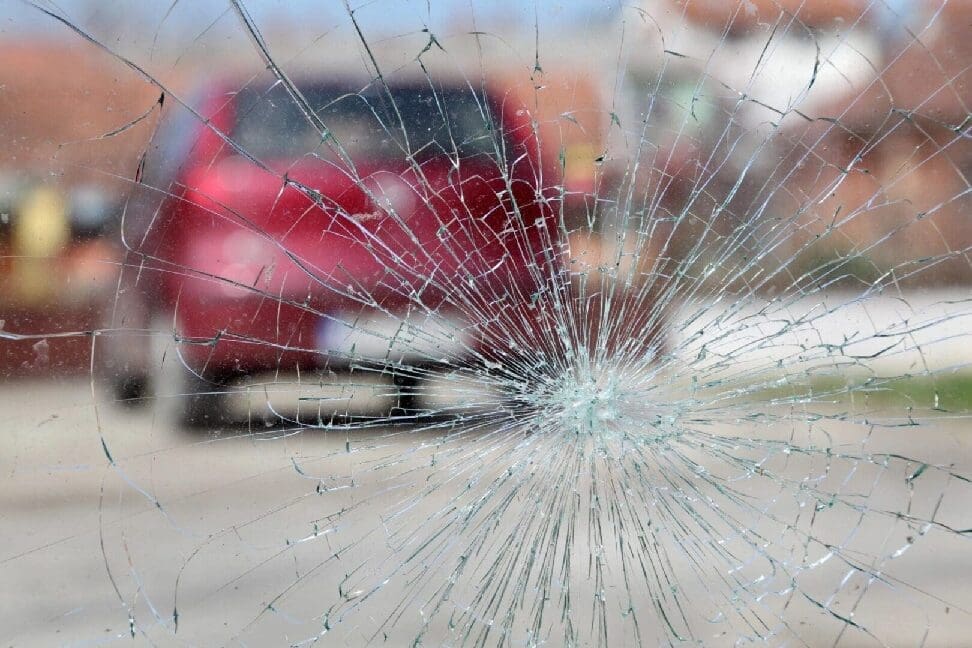 spider-crack-glass-needs-windshield-replacement Red blurred vehicle seen through a spider-cracked glass needing windshield replacement.