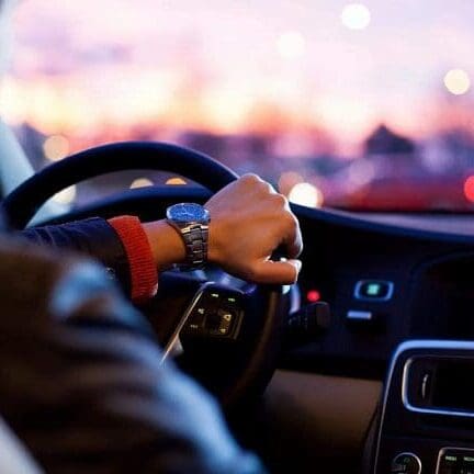 Driving Experience Through Windshield Driver's arm on steering wheel seen through windshield in town setting